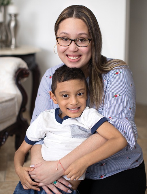Young woman in eyeglasses smiles as she wraps her arms around a smiling young boy.