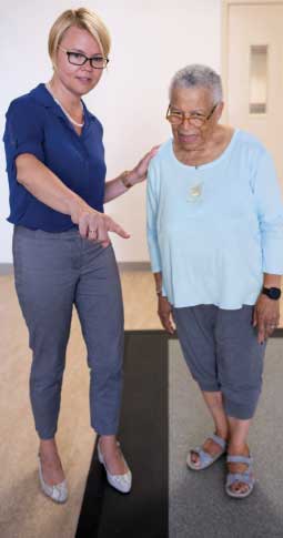 Woman in short blond hair and blue shirt directs older woman in light blue sweater. Both are standing.