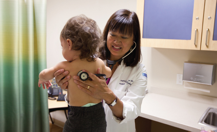Female doctor with stethoscope on toddler's back.