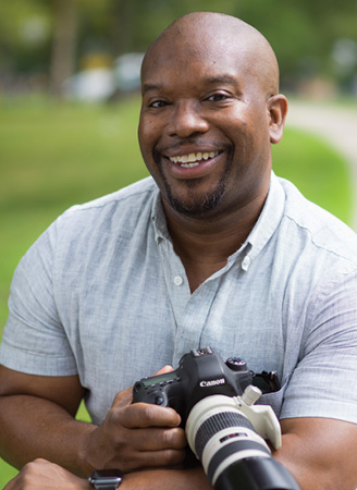 Smiling young man holds camera.