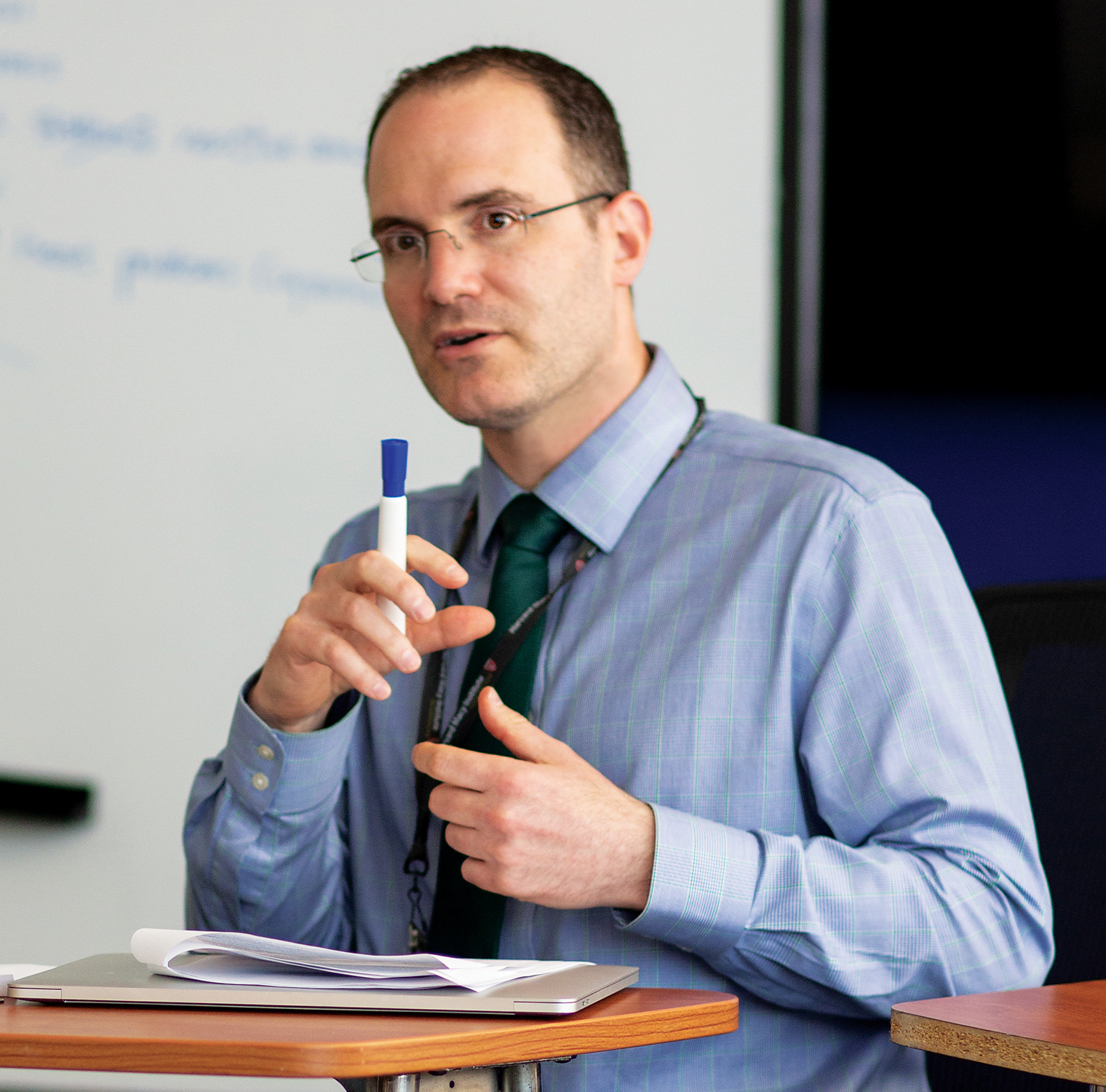 Man in blue shirt gestures with whiteboard marker in hand.